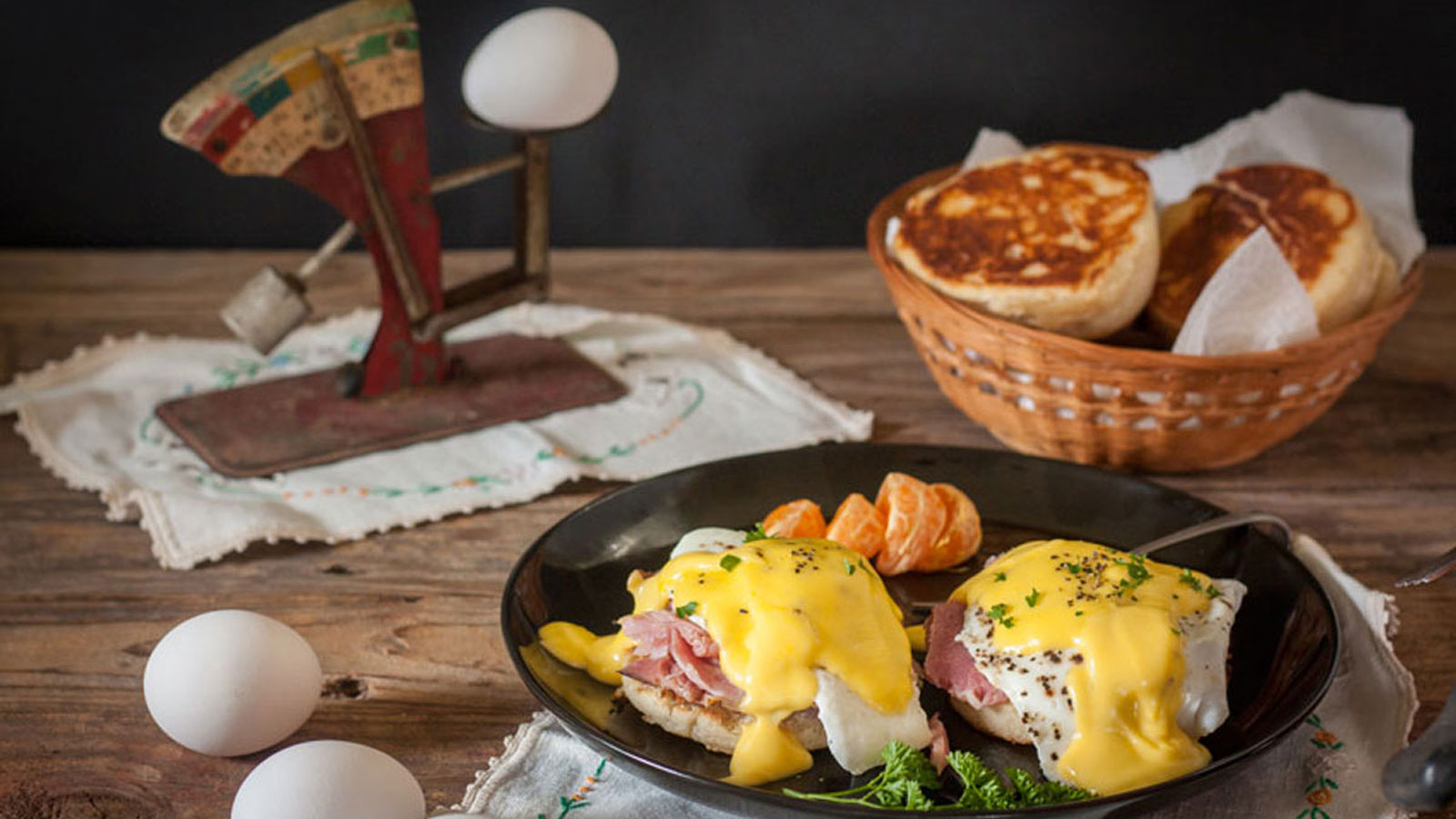 Eggs benedict on a black plate topped with creamy hollandaise sauce.