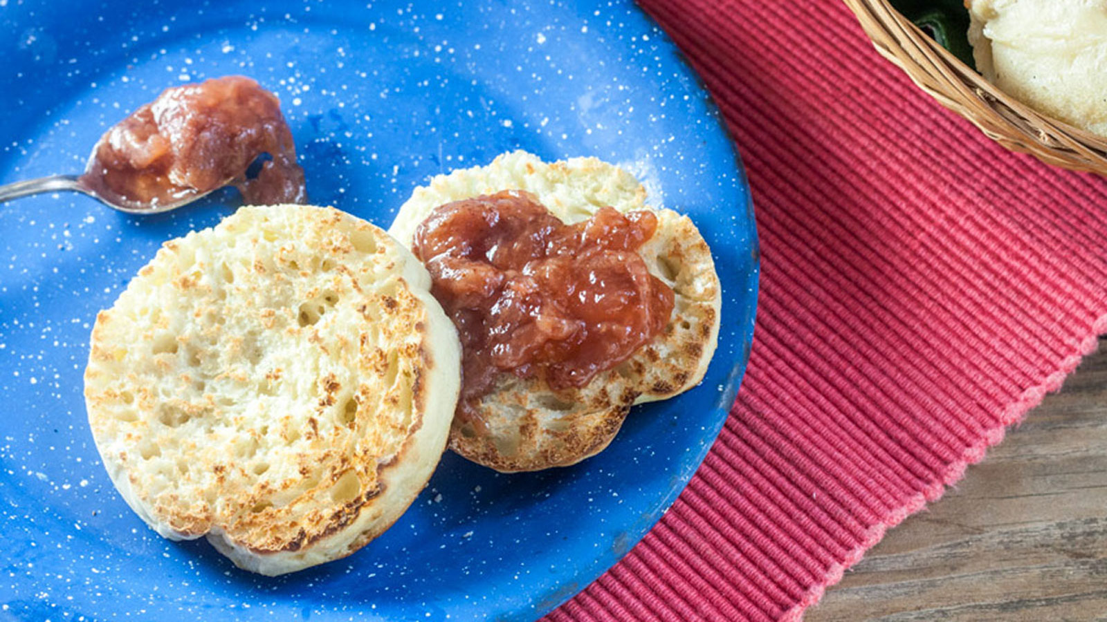Toasted english muffin and silver spoon of jam on blue plate