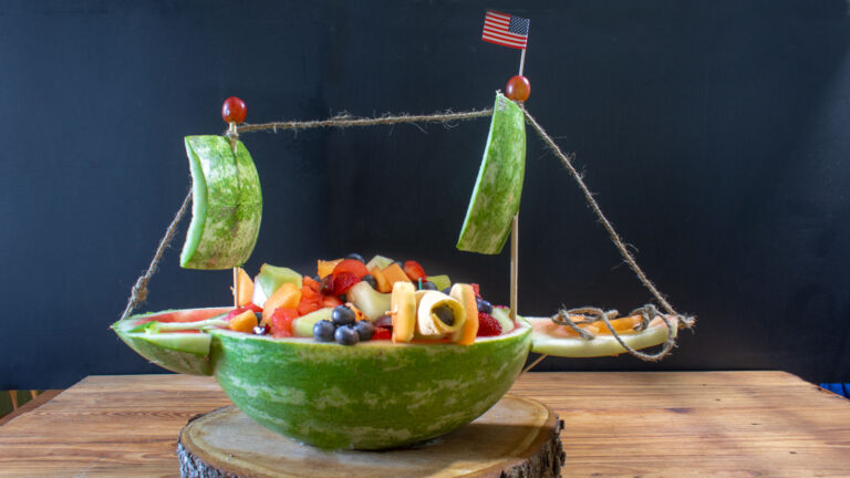 Fruit salad served in a bowl made from a watermelon that is carved in the shape of aaa pirate ship.