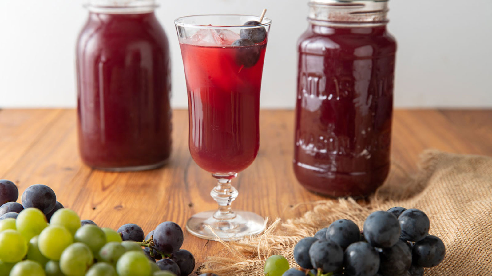 Grape juice in a fluted glass next to jars of canned Grape juice.