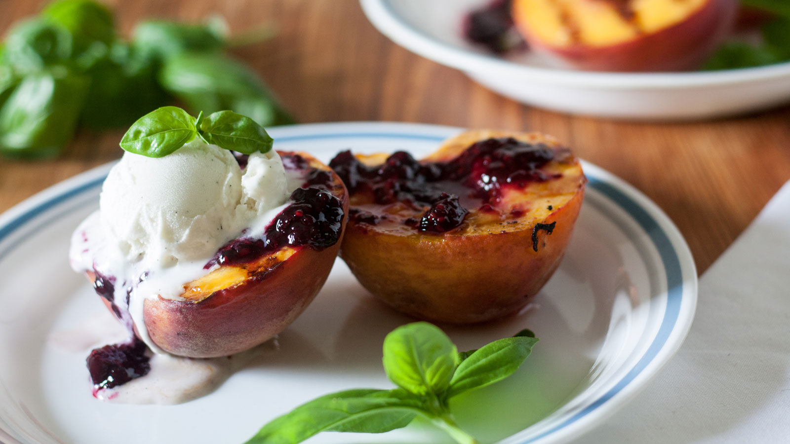 Ice cream topped grilled peaches with blackberry sauce.