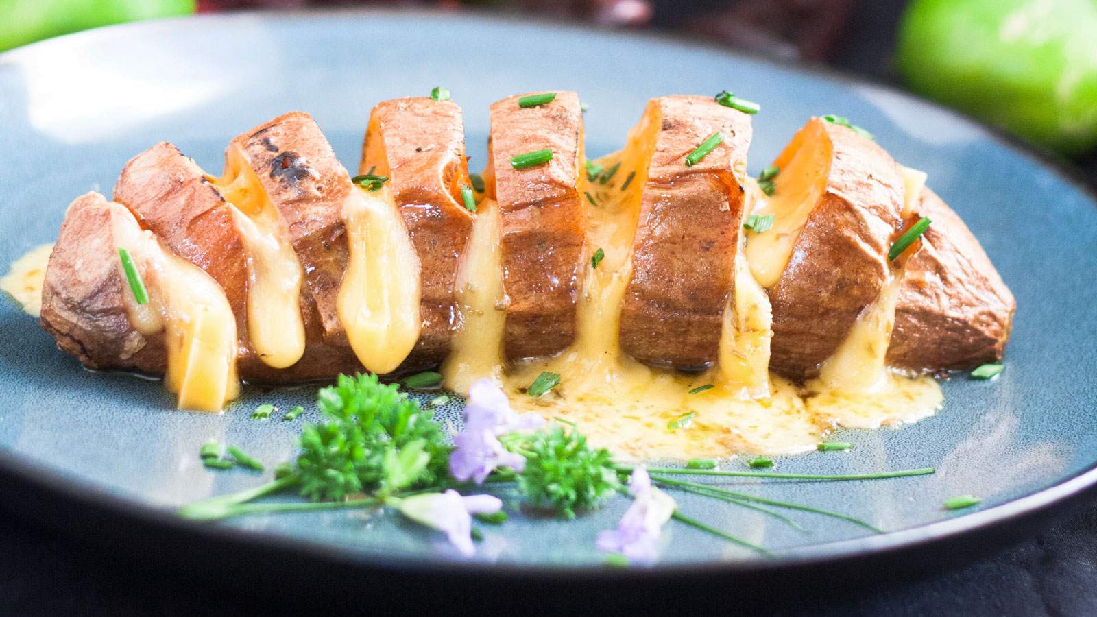 Cheesy hasselback sweet potato on blue plate.