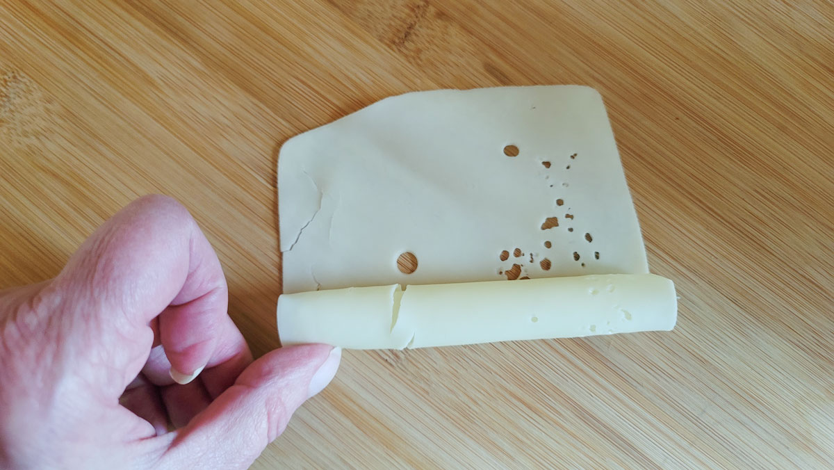 Rolling sliced cheese into a log.
