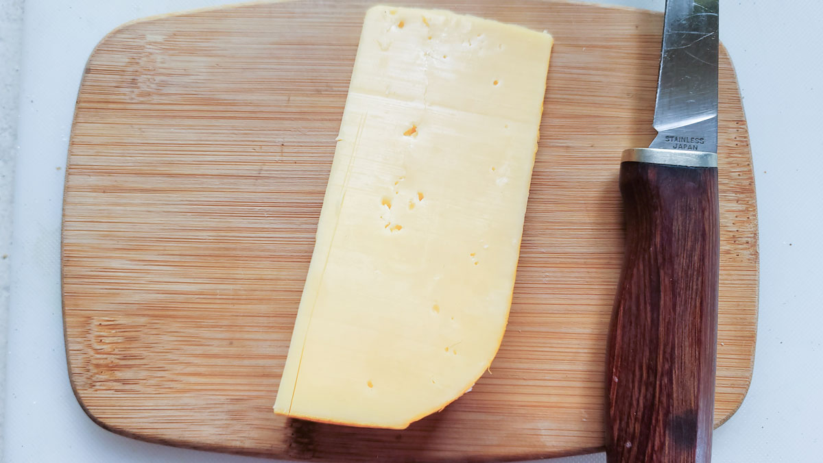 Wedge of cheese on its side on a cutting board.