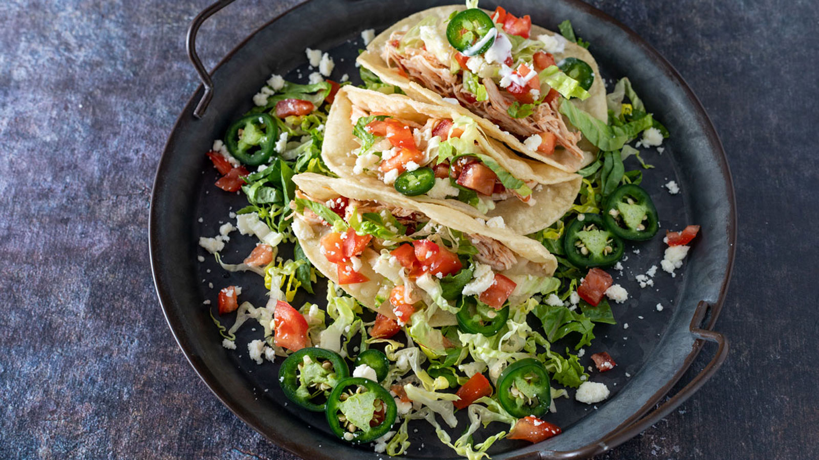 Chicken tacos on a metal tray with colorful fixings.