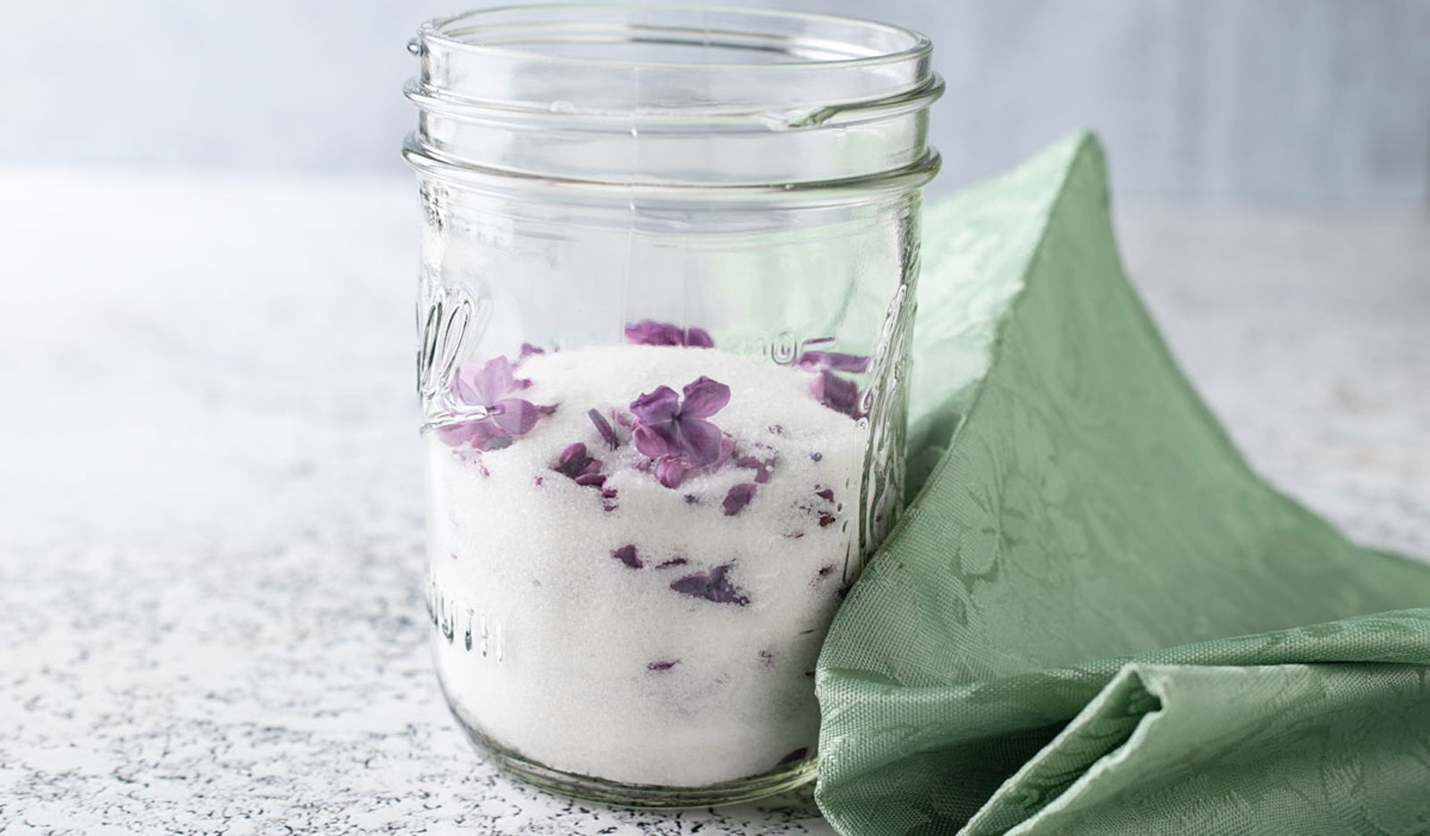 Lilac sugar in a jar with purple petals.