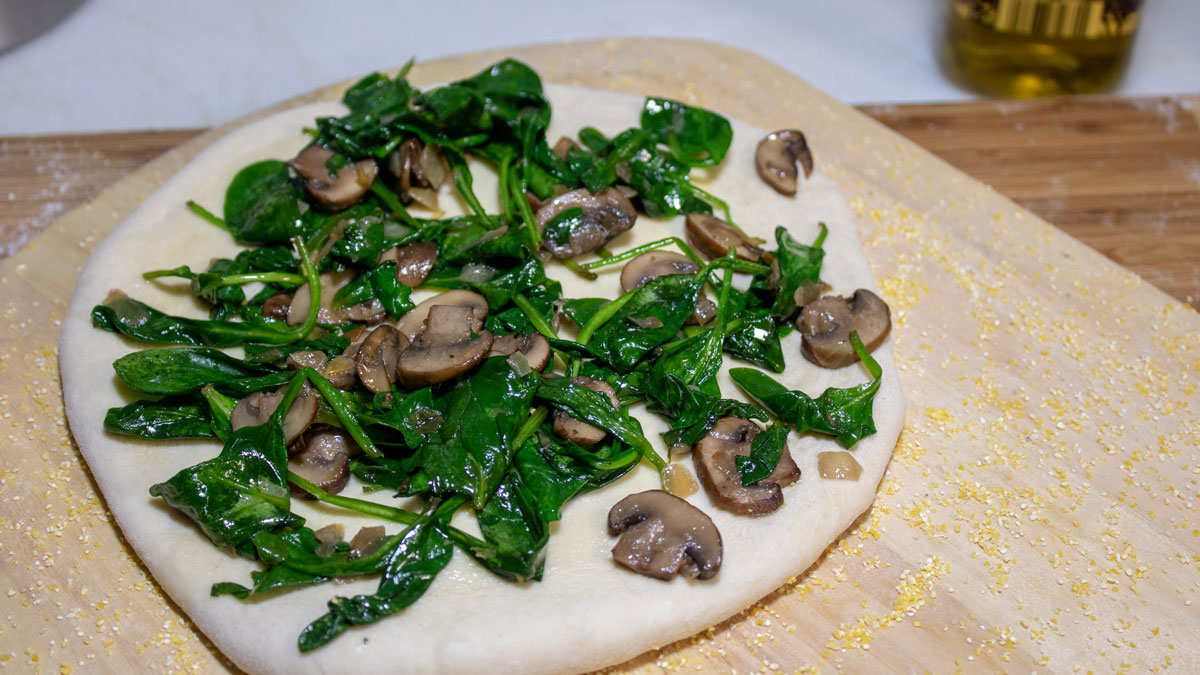 Spinach and mushroom mixture spread on top of the pizza.