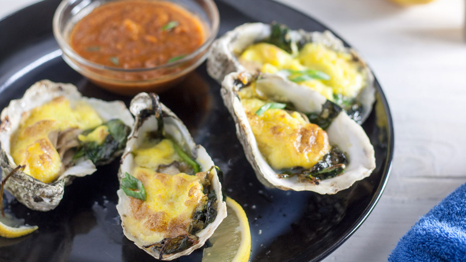 Oysters Rockefeller with Hollandaise sauce on a black plate.