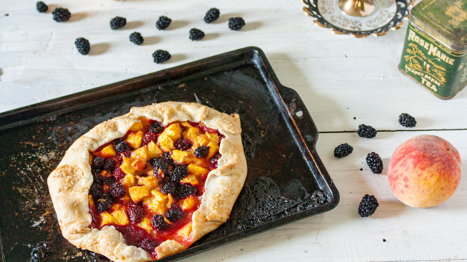 Rustic peach and blackberry galette on baking sheet.