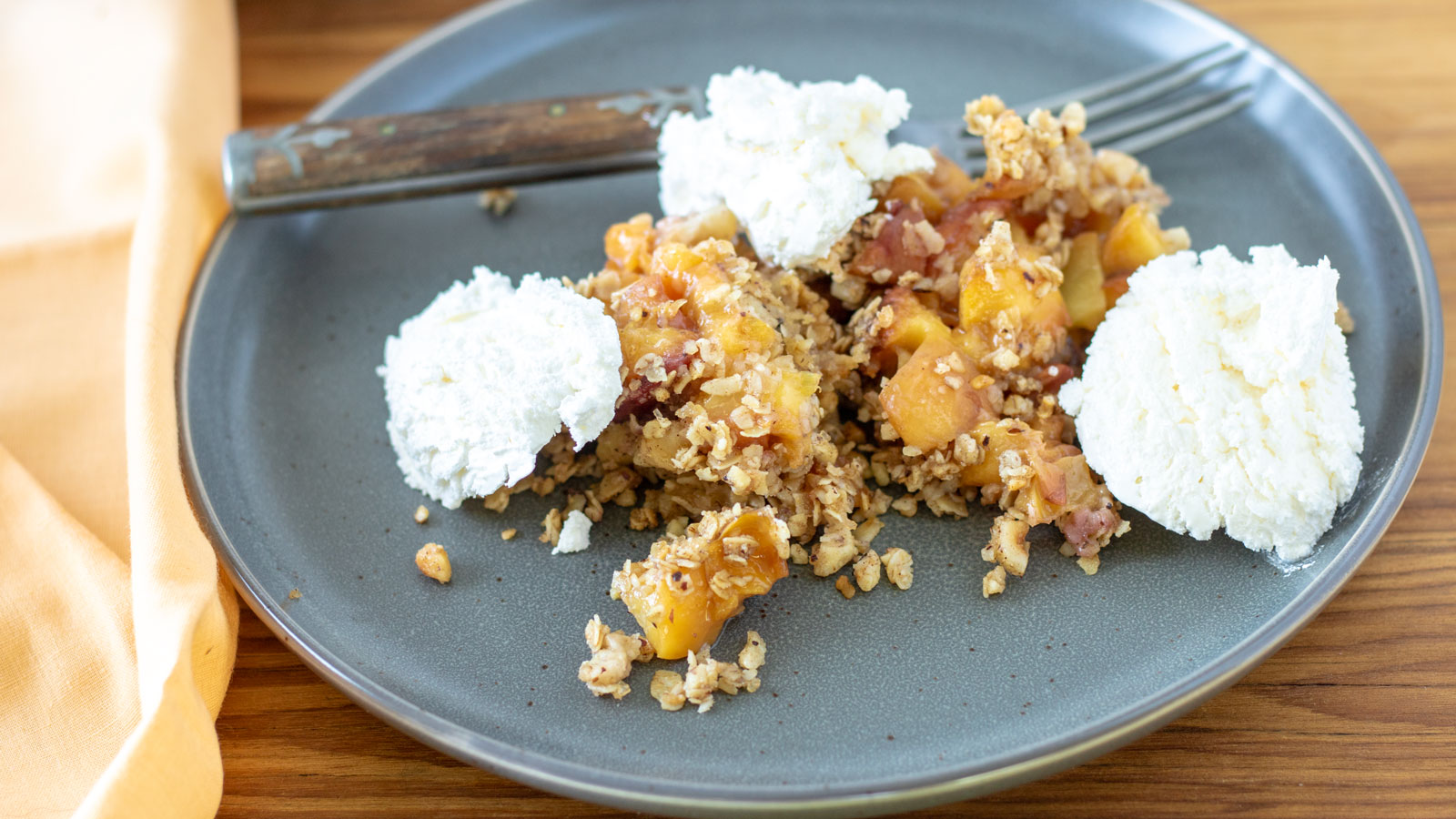 Peach crisp with whipped crem on gray plate.