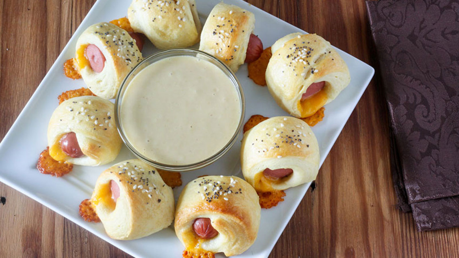 Pigs in a blanket with honey mustard dipping sauce on square white plate.