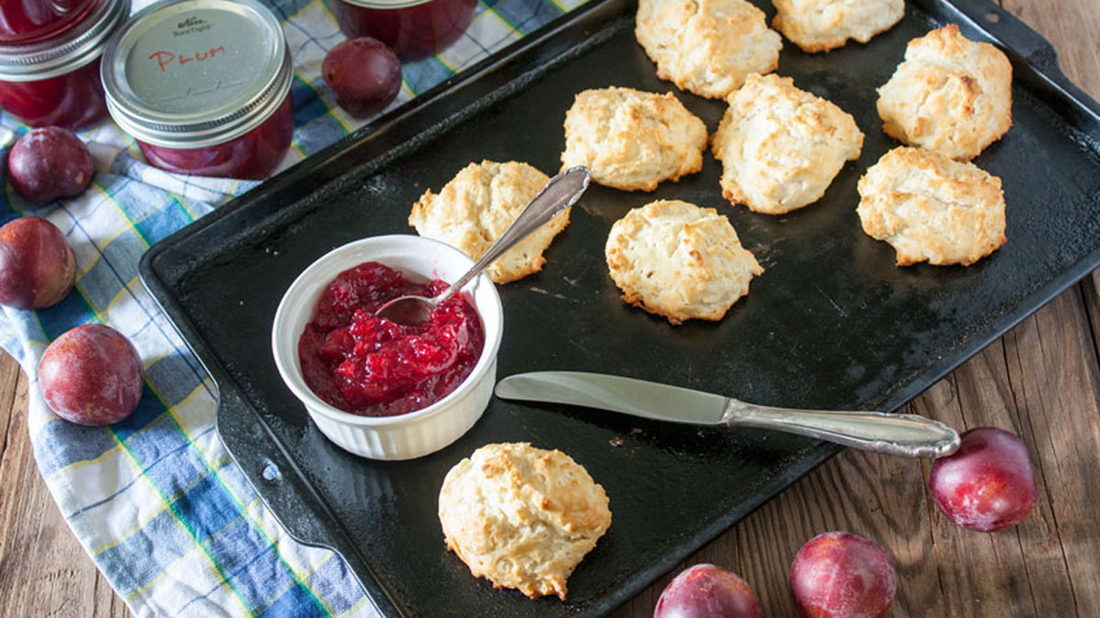 Plum jam in white bowl on antiques baking sheet with biscuits
