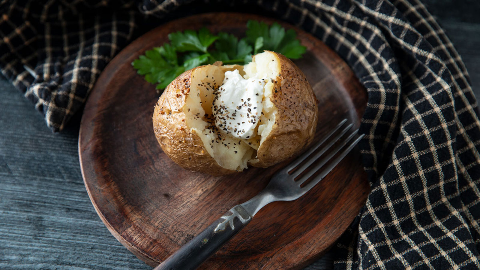 Sour cream topped baked potato on a wooden plate.