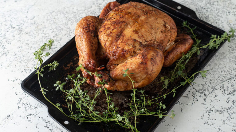 Whole golden brown chicken on an antique metal tray.