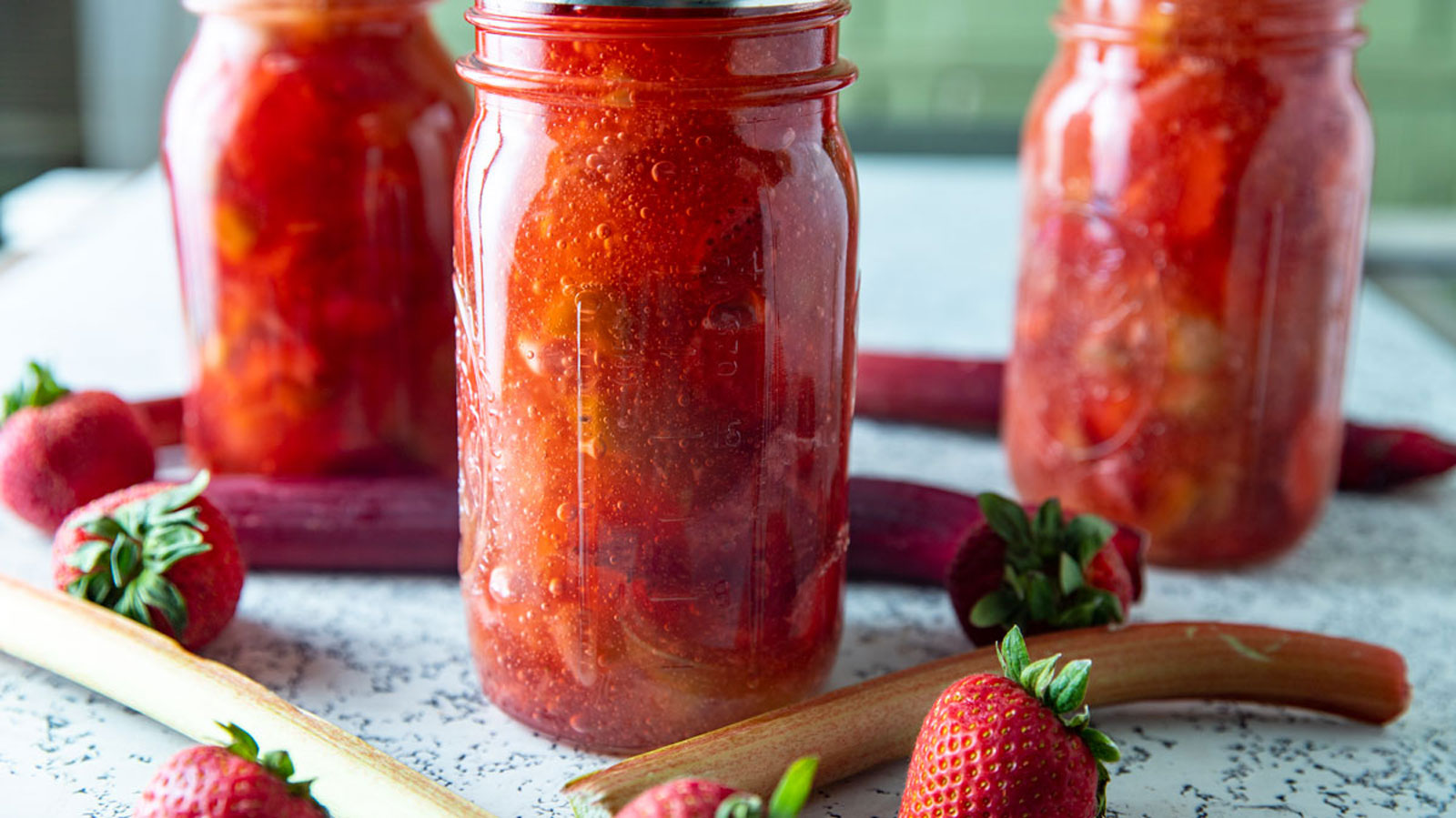 Jars of strawberry rhubarb pie filling with fresh rhubarb and berries.