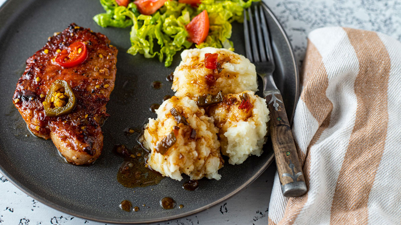 Pork chops on a black plate with side dishes.