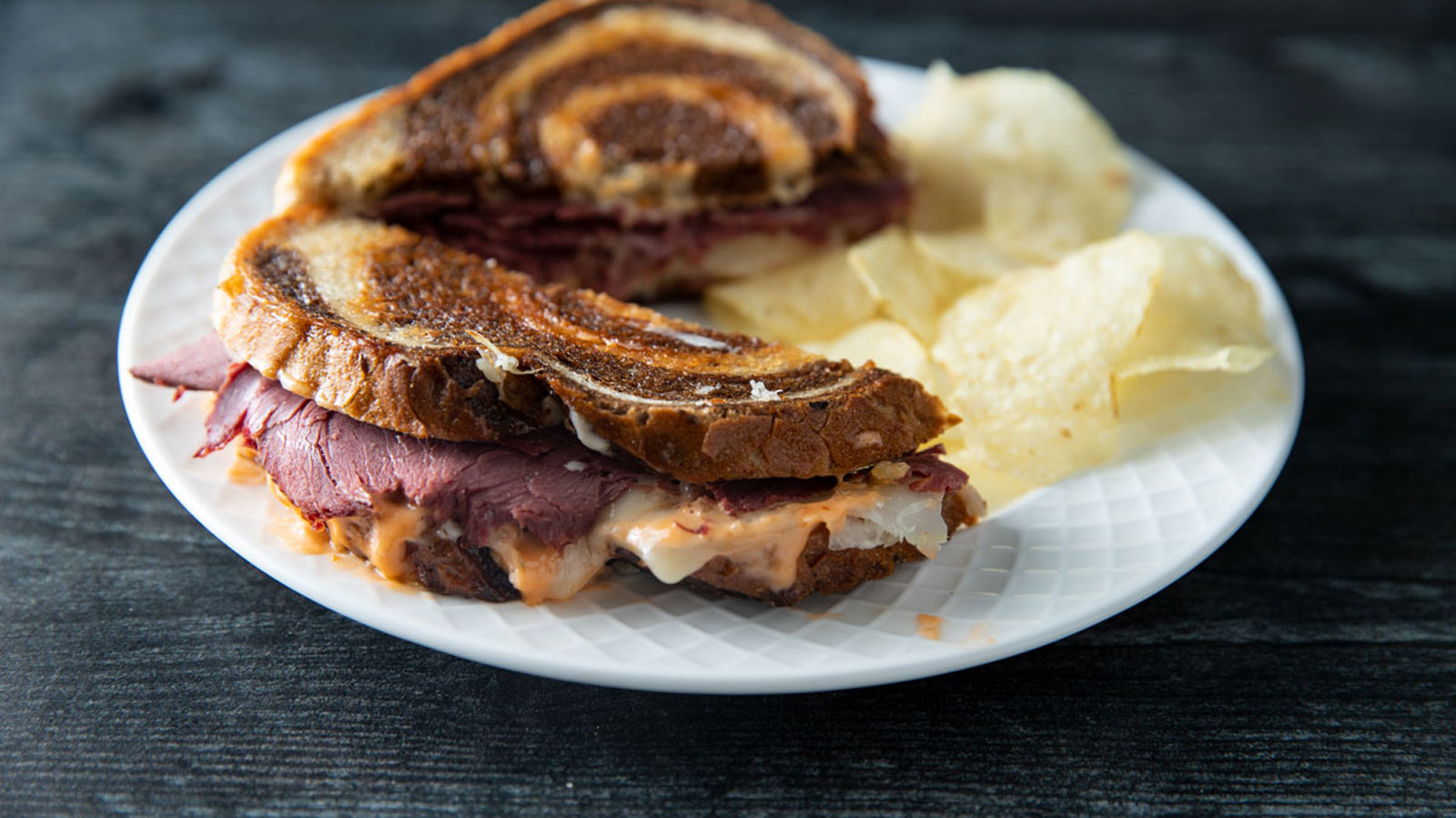 Meaty venison Reuben on a white plate with potato chips.