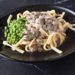 Stroganoff in a black bowl with peas.
