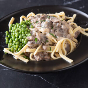 Stroganoff in a black bowl with peas.