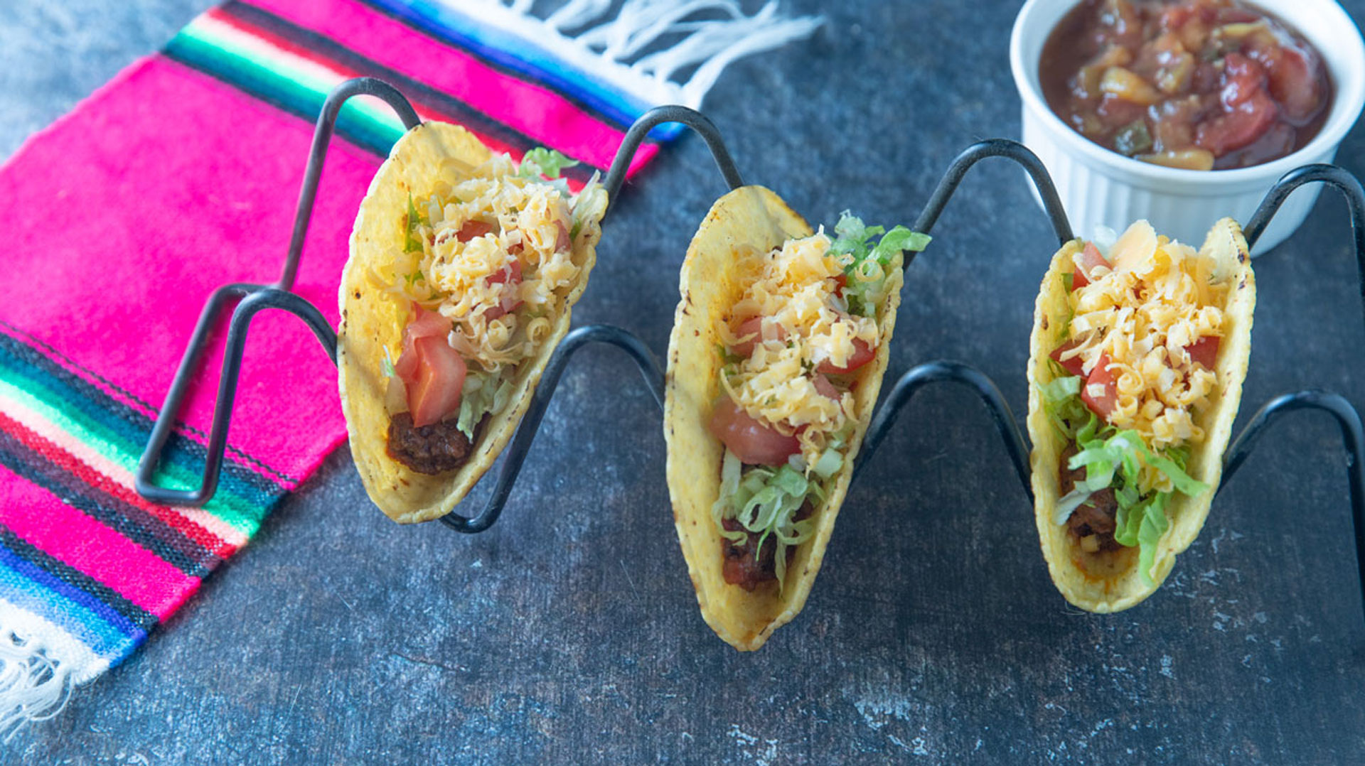 Three ground beef tacos with lettuce tomato and cheese topping.