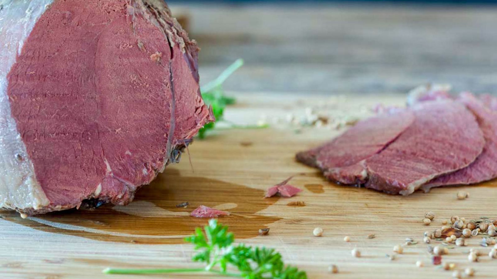 Sliced corned venison on a cutting board with a whole roast.