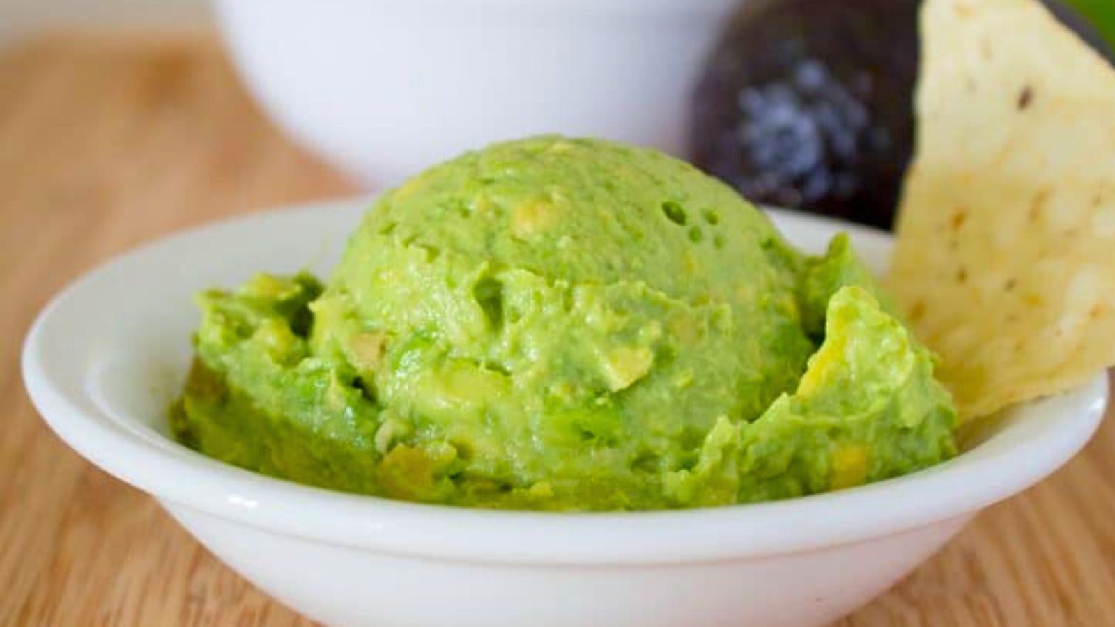 Guacamole in a white bowl with a tortilla chip.