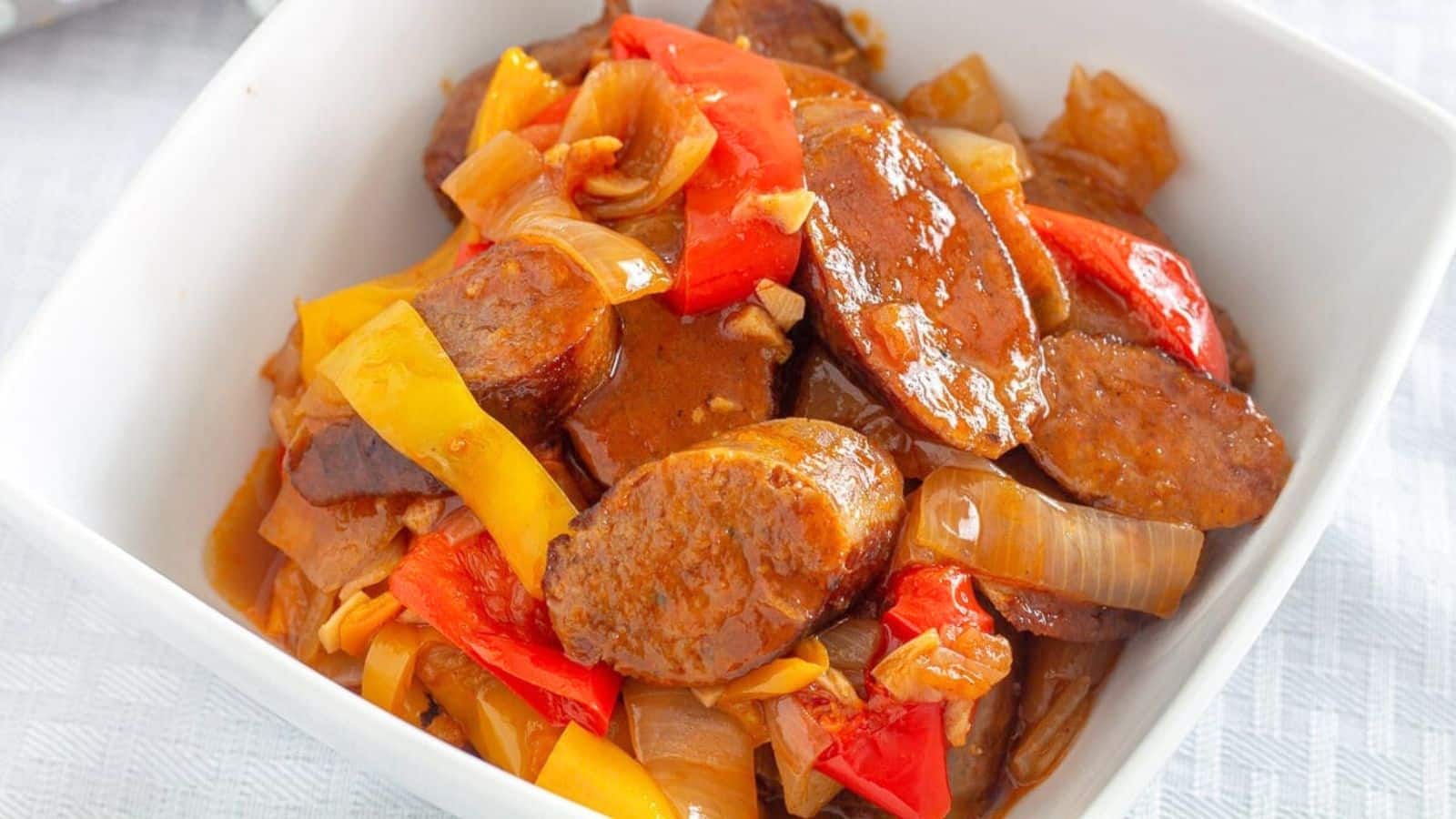 Sliced sausage and colorful peppers in a white bowl.