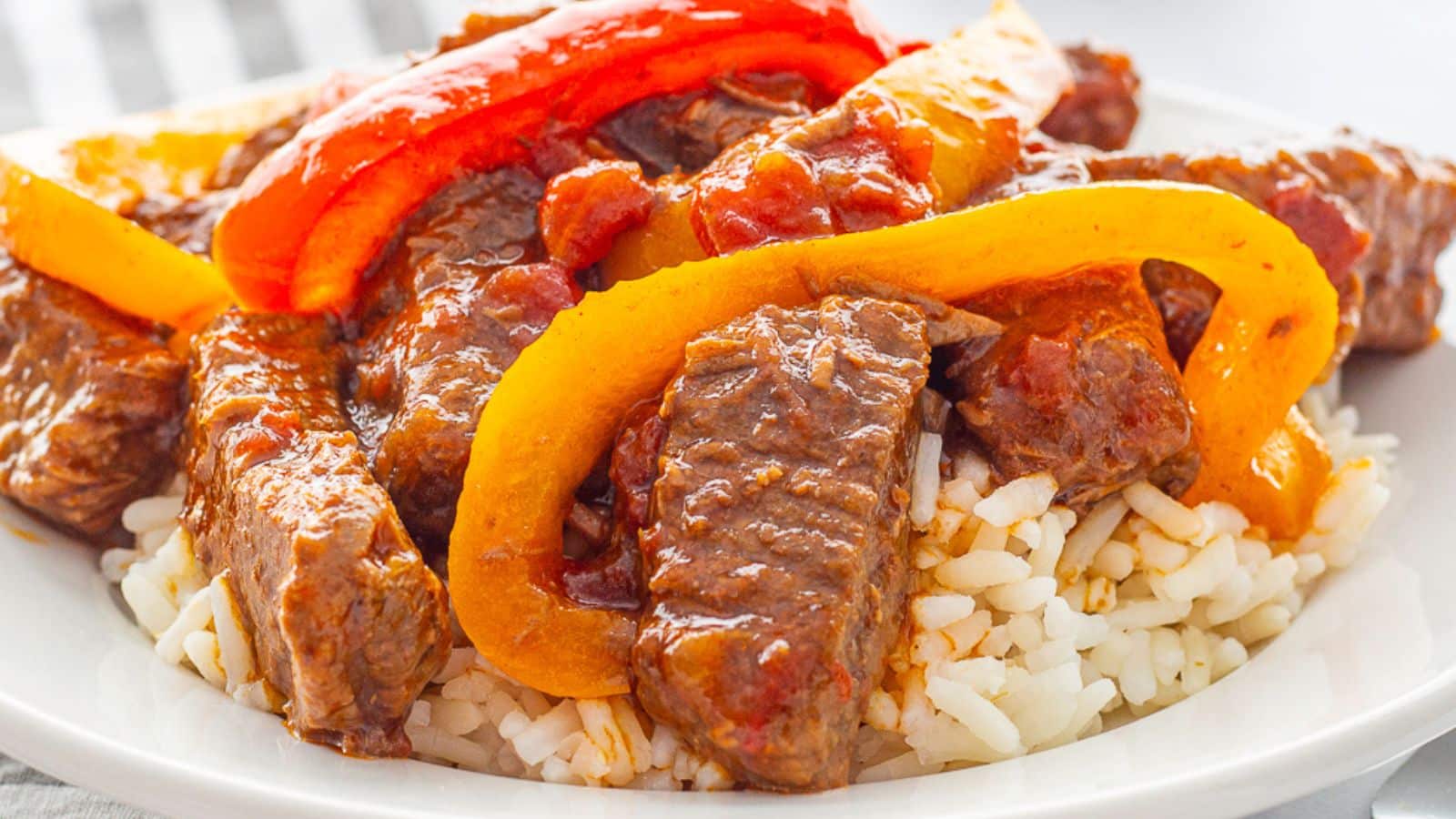 Sliced steak with colorful bell peppers on a white plate.
