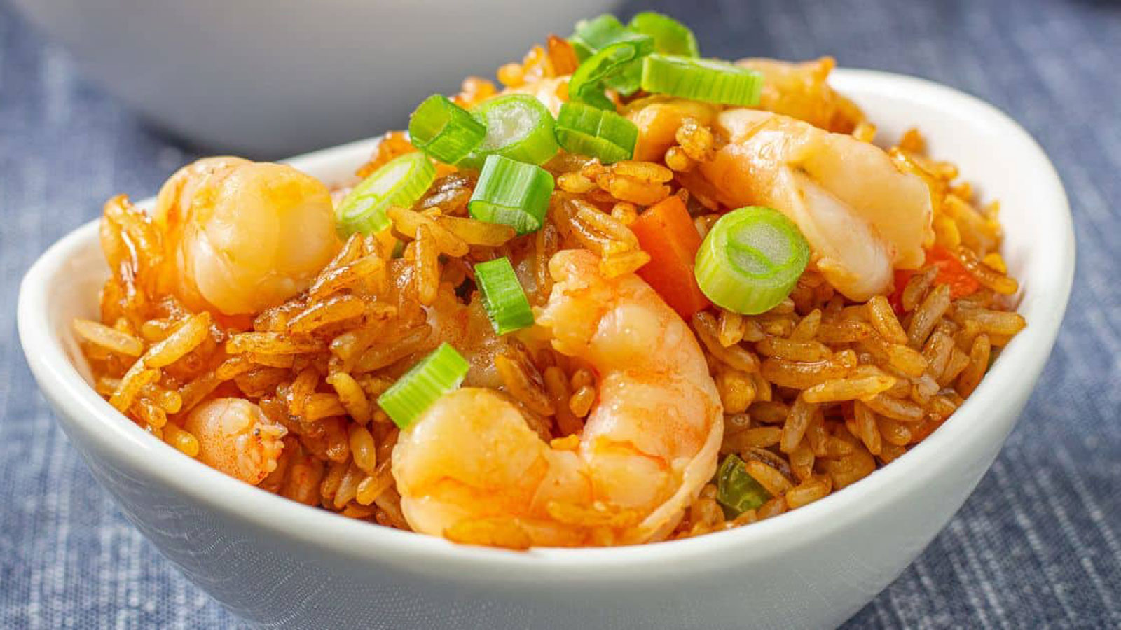 Fried rice in a white bowl topped with shrimp and chopped scallions.