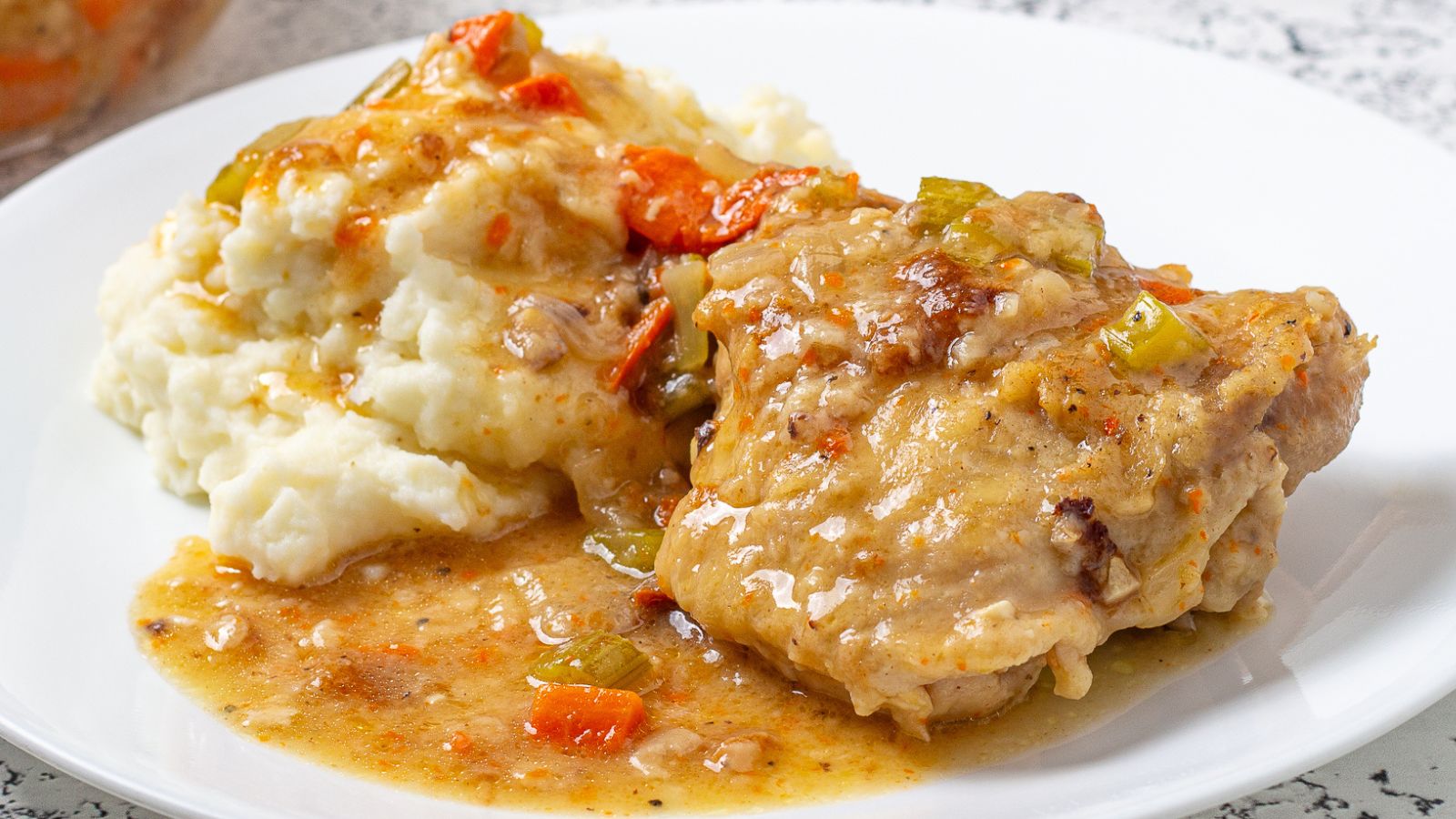 Chicken smothered with sauce on a white plate with potatoes.