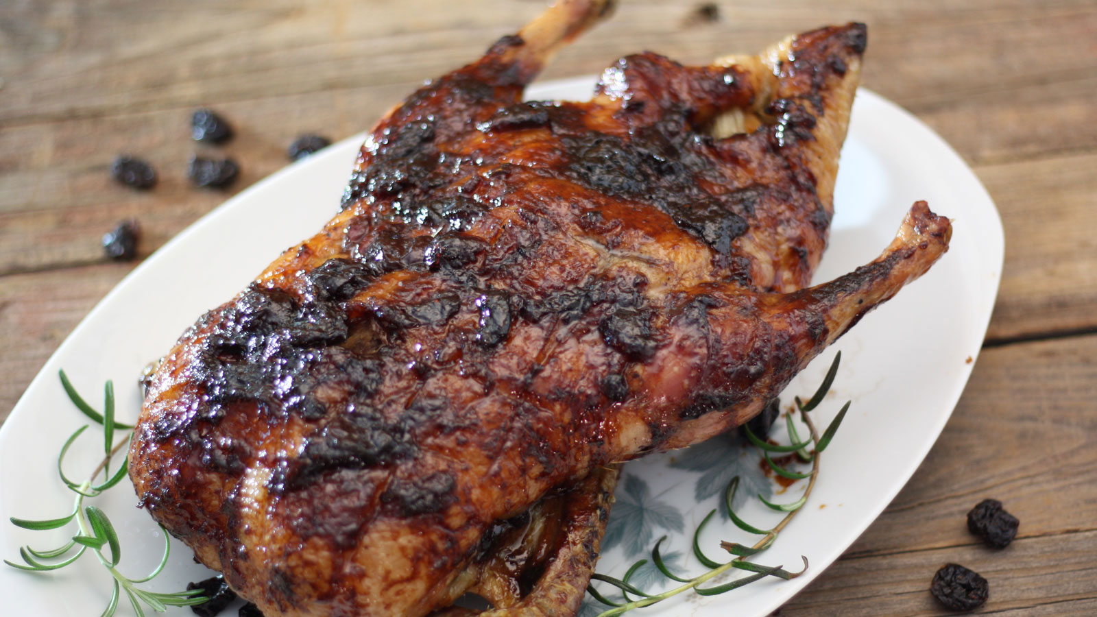 Whole duck slathered with cherry and balsamic reduction on a white platter.