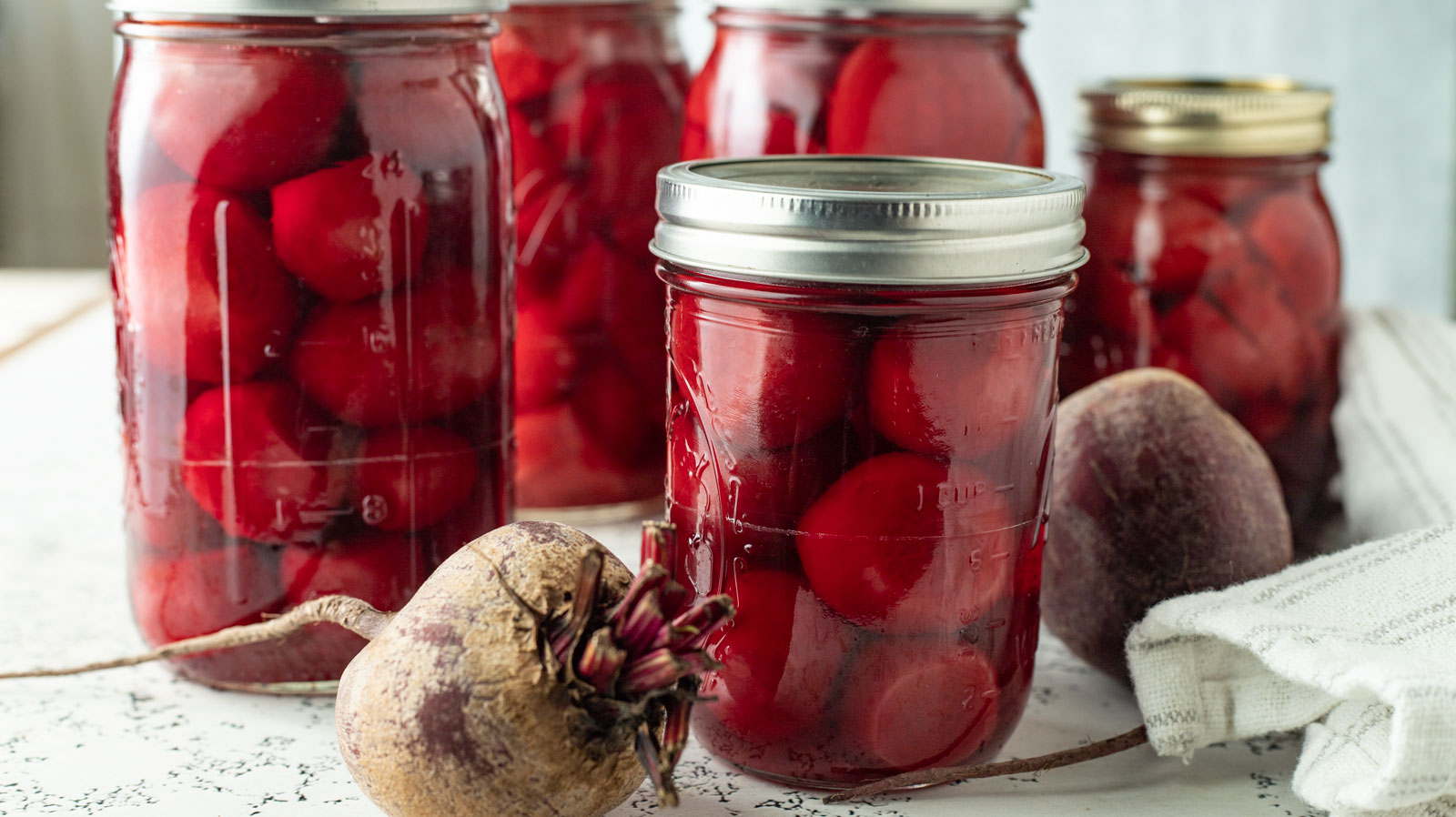 Jars of canned beets with fresh beets in the foreground.