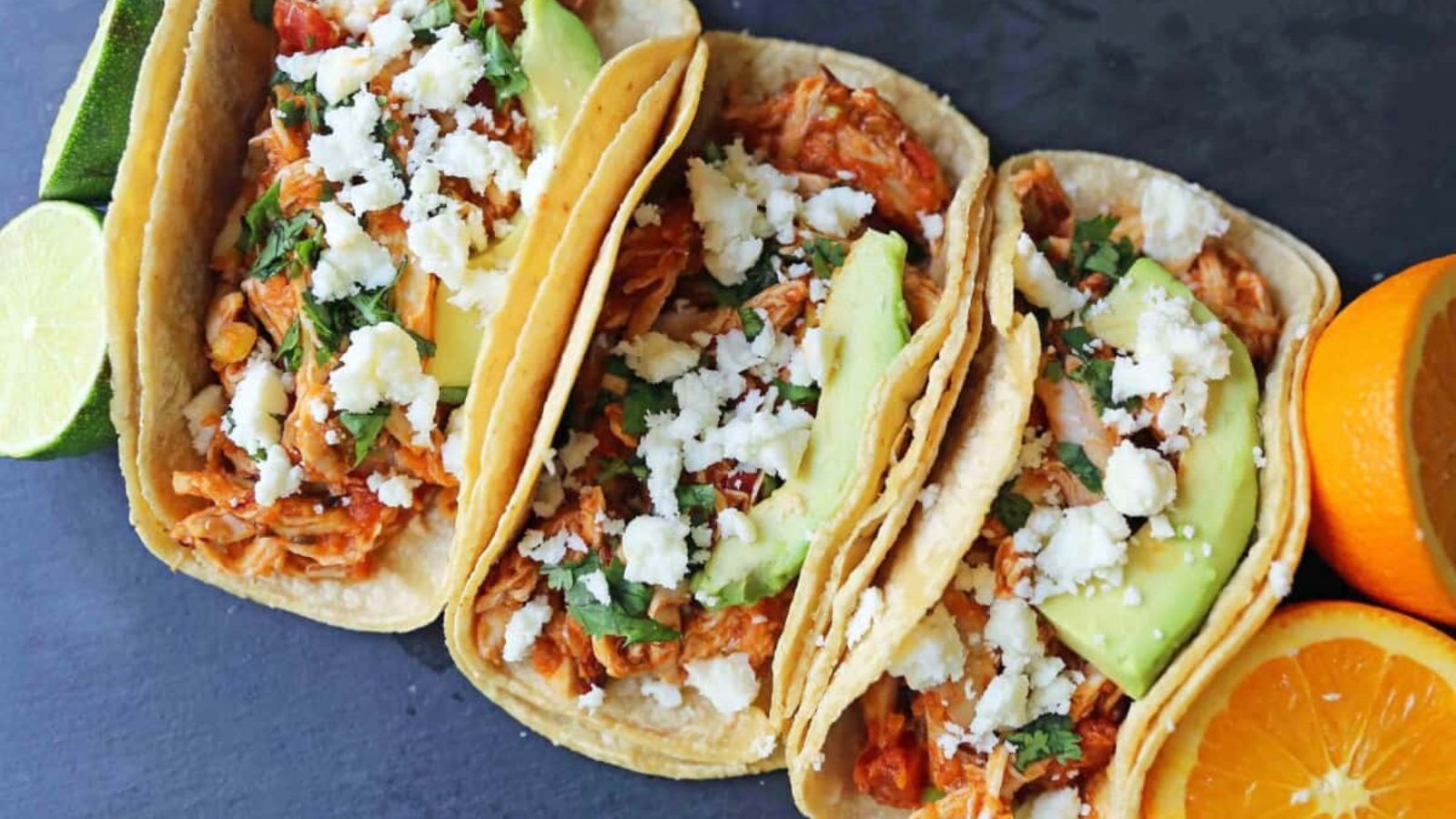 Three tacos lined up on a dark background.