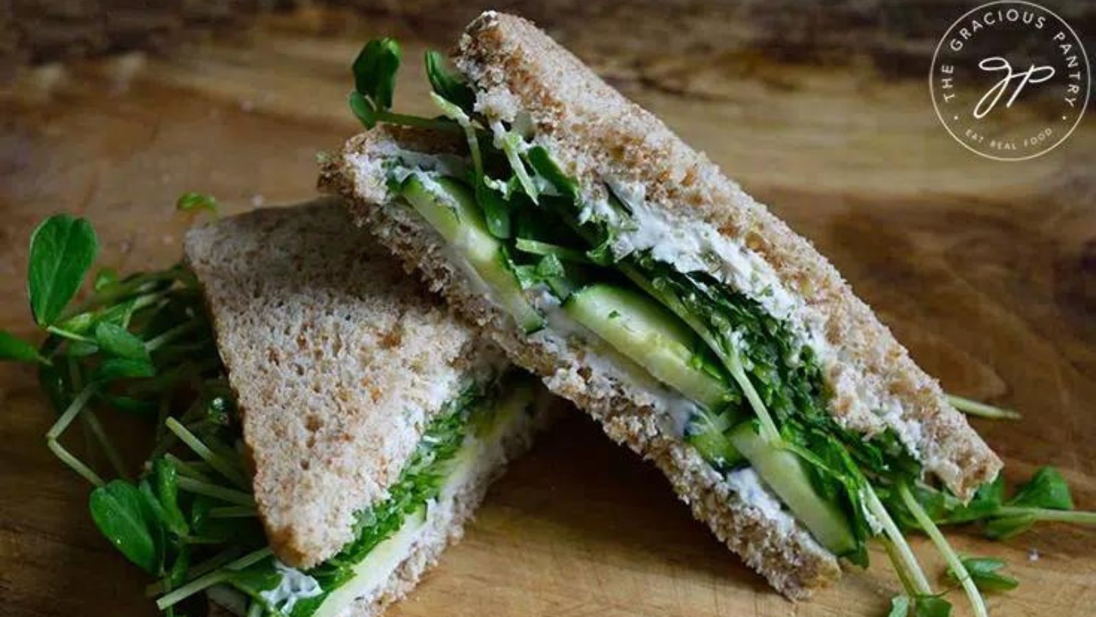 Halved cucumber sandwich on a wooden board.