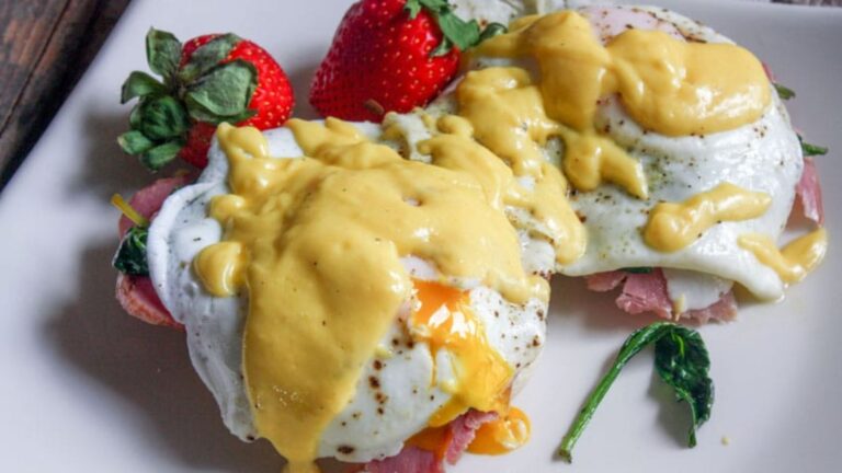 Eggs benedict on white plate with broken yolks.