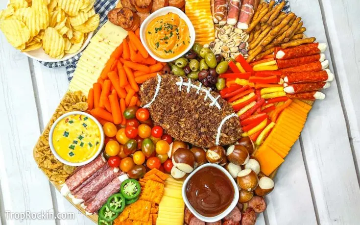 Cheese ball in the shape of a football with meats and cheeses and crackers on a cutting board.