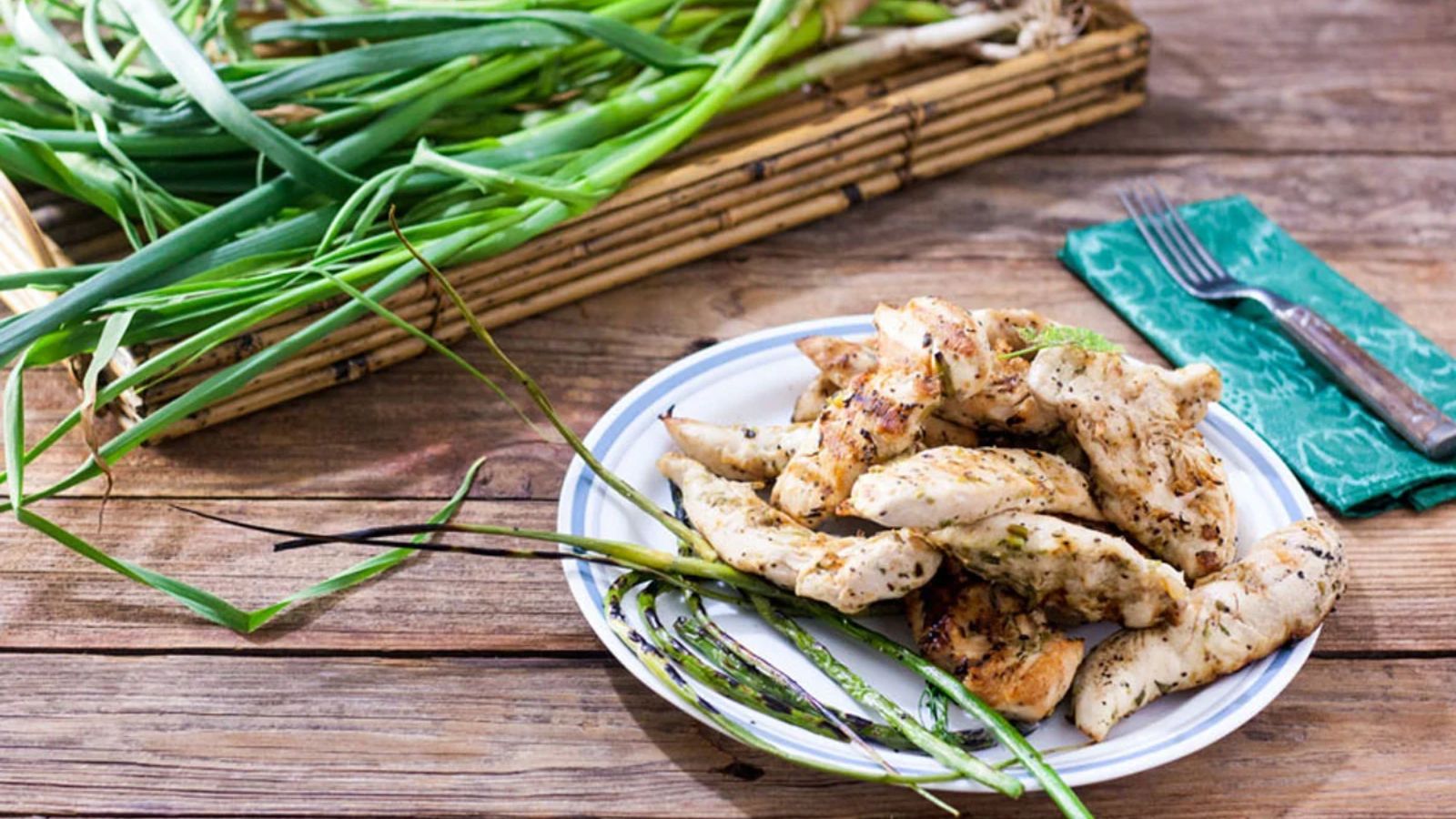 Grilled chicken tenders piled on plate with grilled garlic scapes.