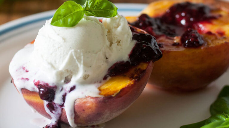 Grilled peach topped with blackberry sauce and a scoop of ice cream.
