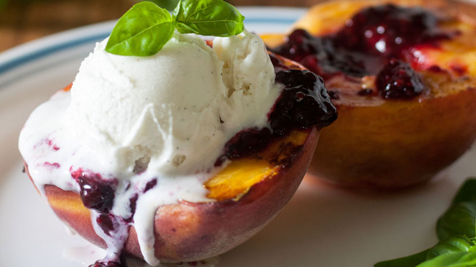 Grilled peach topped with blackberry sauce and a scoop of ice cream.