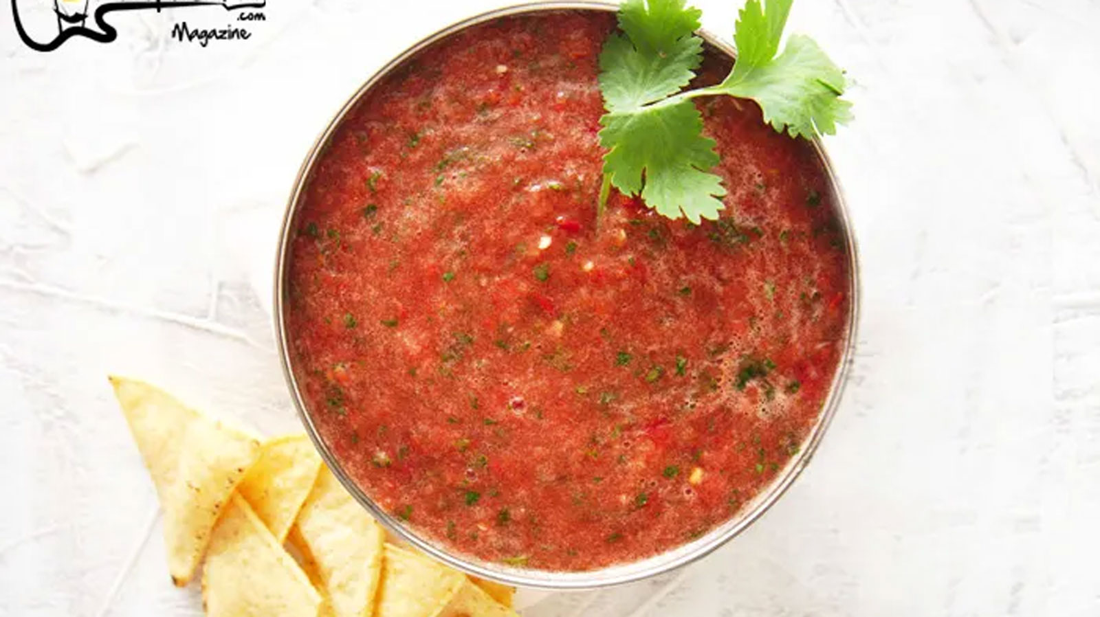 Bowl of red salsa on a white board with cilantro garnish.