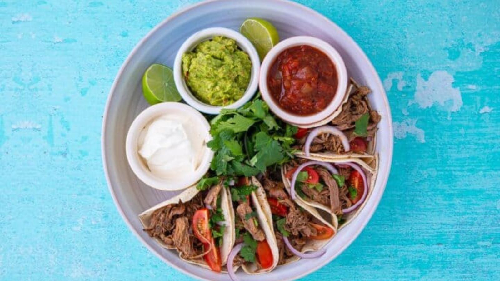 Large plate with toppings and lamb tacos.