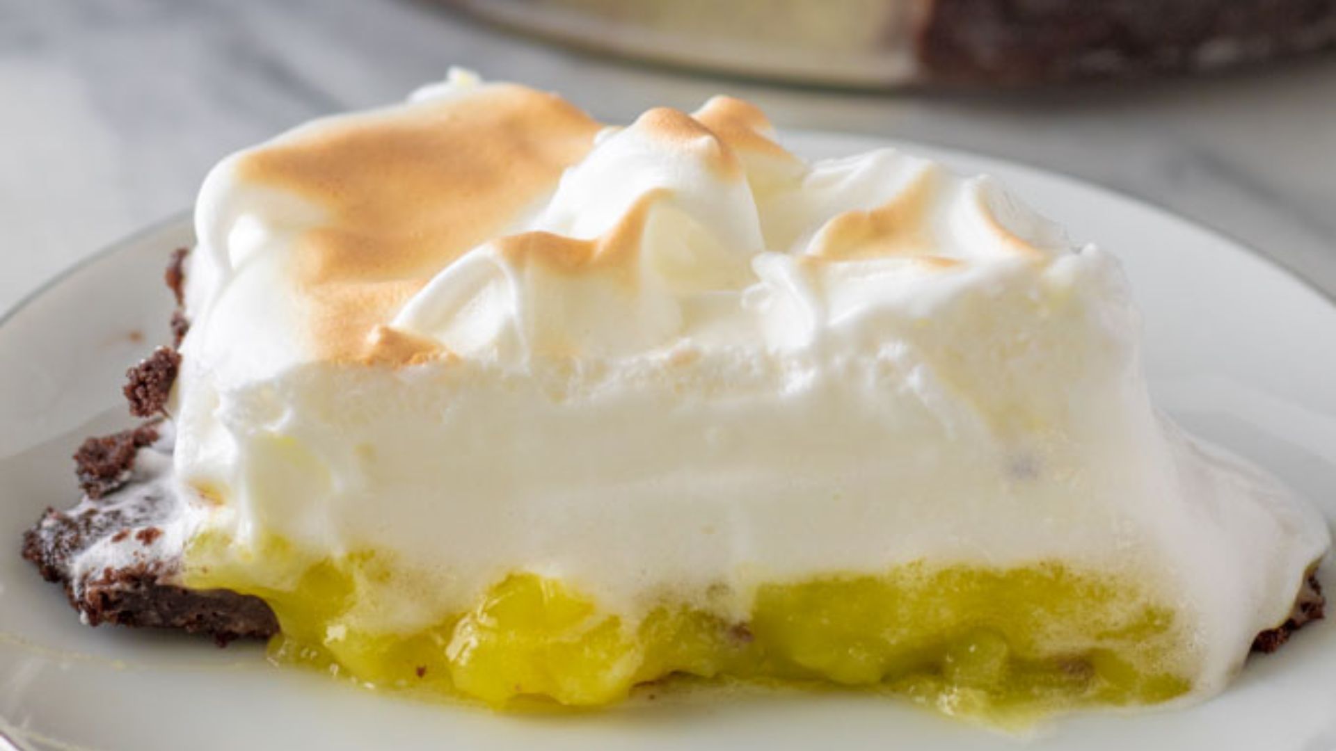 Slice of lemon meringue pie on a white plate.