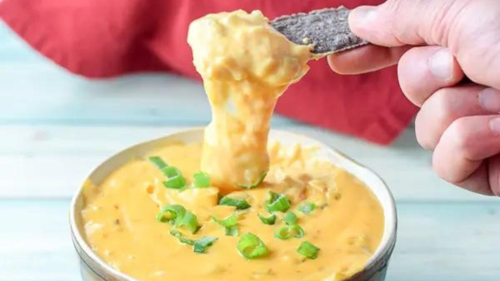 Woman's hand scooping dip out of bowl with a tortilla chip.
