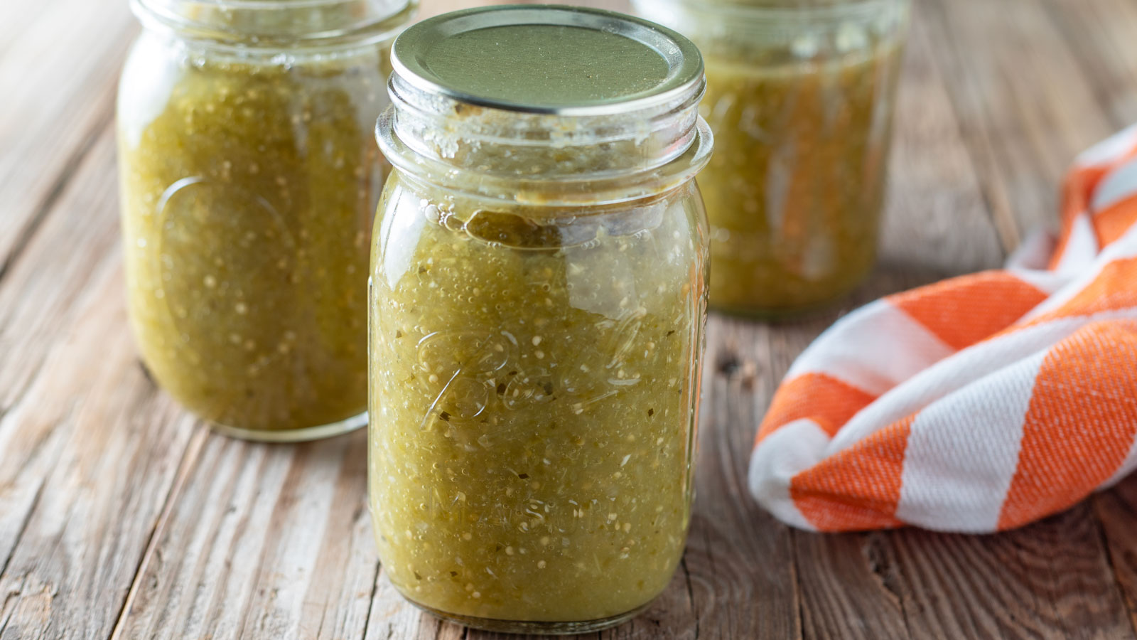 Jars of salsa verde on a barn wood slab.