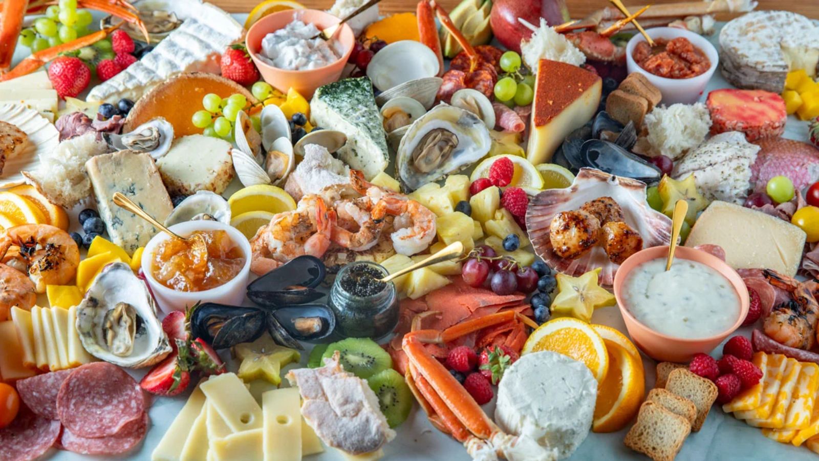 Board loaded with seafood, meats, fruits and breads.