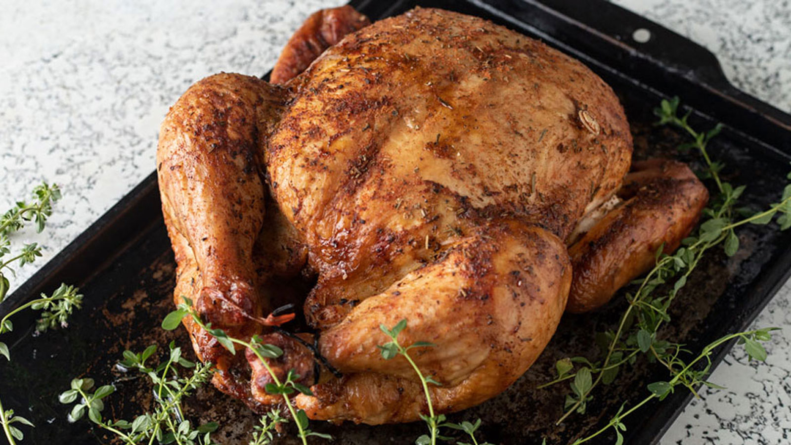 Whole chicken on a black tray with fresh thyme branches.