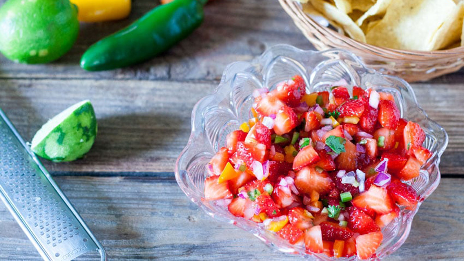 Colorful strawberry salsa in clear bowl with basket of chips.
