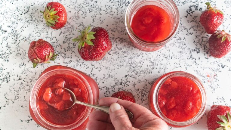 Woman's hand scooping strawberry sauce out of a jar with a spoon.
