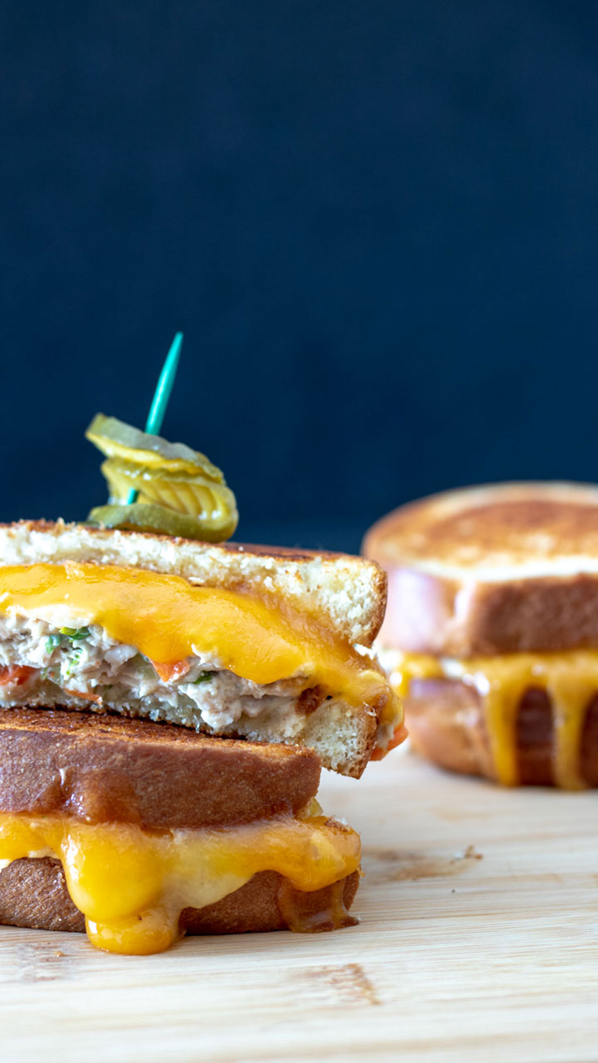 Tuna sandwich cut in half with cheese dripping.