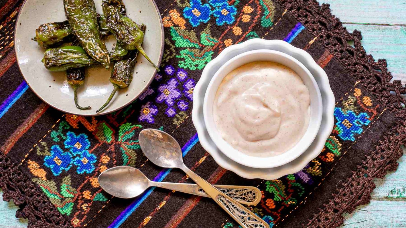 Bowl of dip next to peppers on a tapestry.